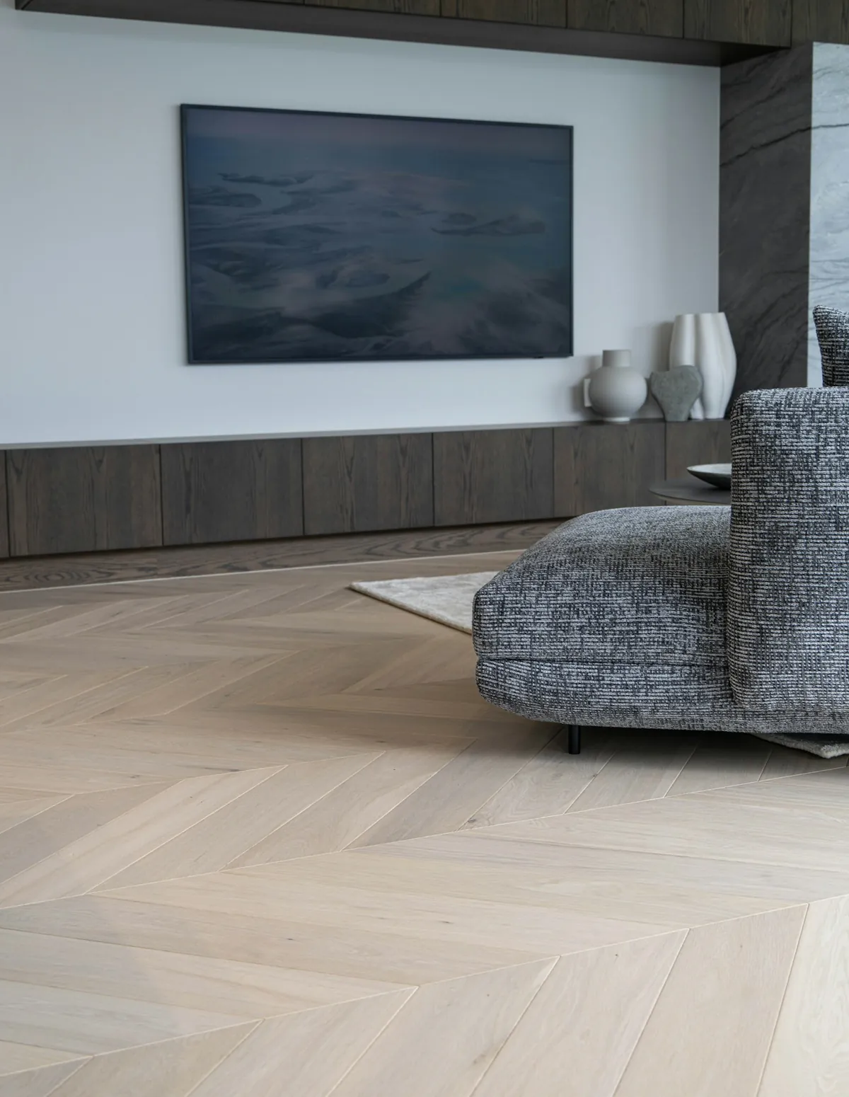 Living room with pale herringbone wood floor and dark joinery
